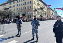 Невский проспект в Петербурге перекрыт для проезда, на тротуарах давка. Петербуржцы, которые вышли в центр увидеть парад, смотрят его на своих смартфонах или на городском экране с мигающим цветокором